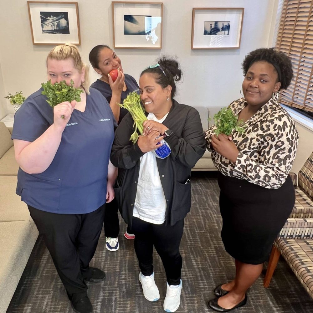 A group of dental team members holding fresh herbs and vegetables, highlighting natural ways to improve breath instead of relying on mints – do tic tacs help with bad breath