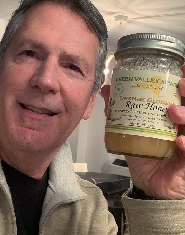 A man holding a jar of raw honey while smiling, representing the question of whether natural sweeteners like honey can contribute to tooth decay – does honey cause tooth decay