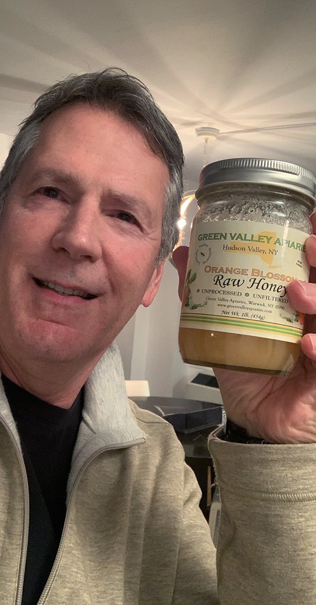 A man holding a jar of raw honey while smiling, representing the question of whether natural sweeteners like honey can contribute to tooth decay – does honey cause tooth decay