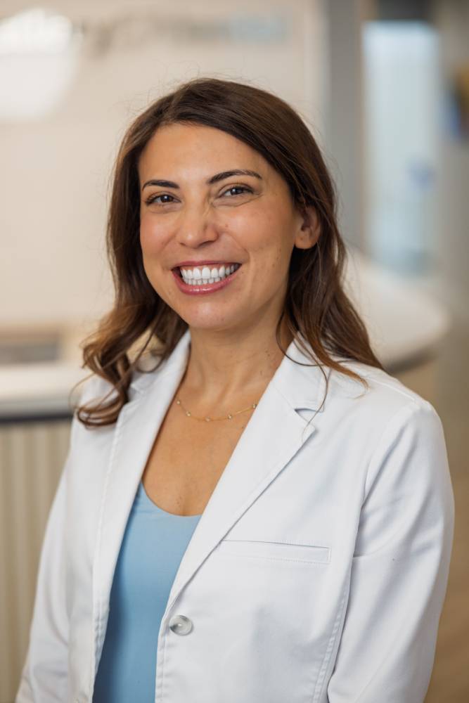 Portrait of Dr. Rebecca Koenigsberg smiling in a white coat inside a modern dental office – Andrew Koenigsberg
