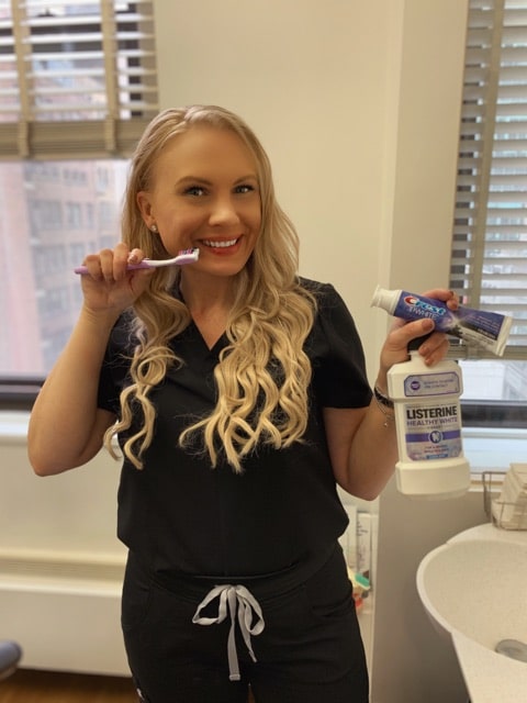 A smiling dental professional holding a toothbrush, toothpaste, and mouthwash in a dental office while discussing Marshmallow Meadows teeth whitening reviews – marshmallow meadows teeth whitening reviews