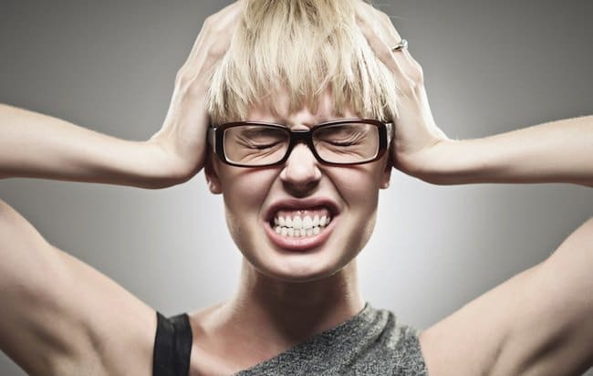 Woman wearing glasses gripping her head and clenching her teeth, illustrating jaw tension and the need to unclench your jaw – unclench your jaw