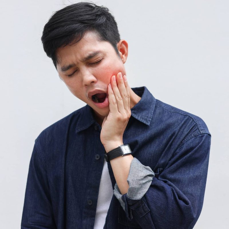 Man holding his jaw in pain with a strained expression, representing facial muscle tension and concerns addressed by EMFACE treatment