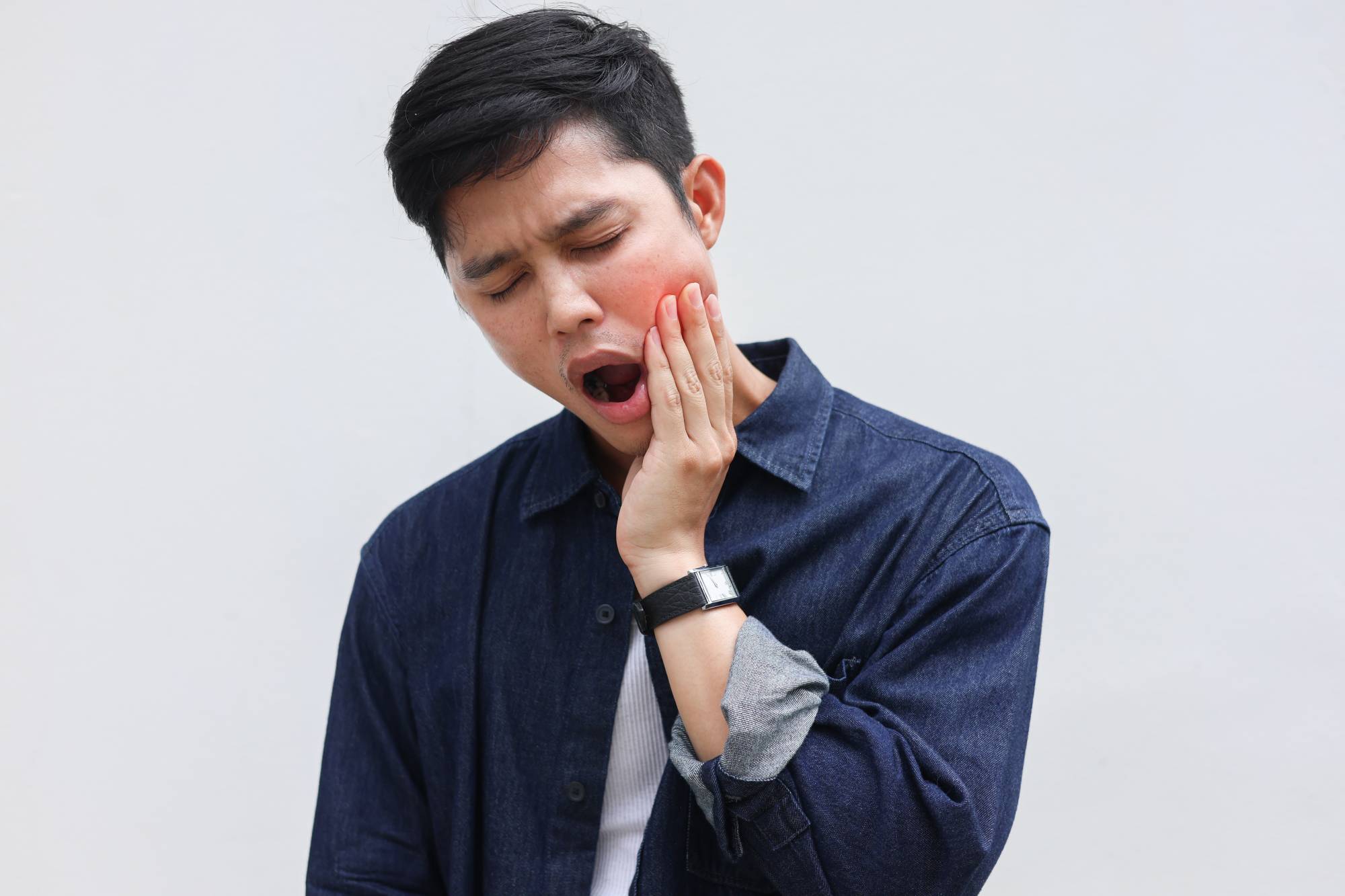 Man holding his jaw in pain with a strained expression, representing facial muscle tension and concerns addressed by EMFACE treatment