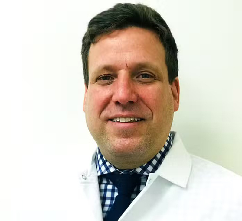 Portrait of Dr. Elan Katz wearing a white coat, checkered shirt, and tie, smiling in a clinical setting – elan katz