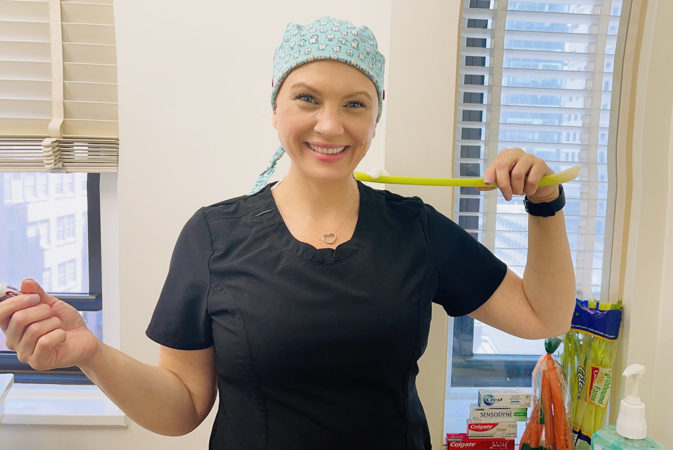 Dental Professional Demonstrating Alternative Tooth Cleaning Method – How to Brush Teeth Without Toothbrush A smiling dental professional holding a long green toothbrush-like tool while standing in a dental office, representing tips on how to brush teeth without toothbrush – how to brush teeth without toothbrush